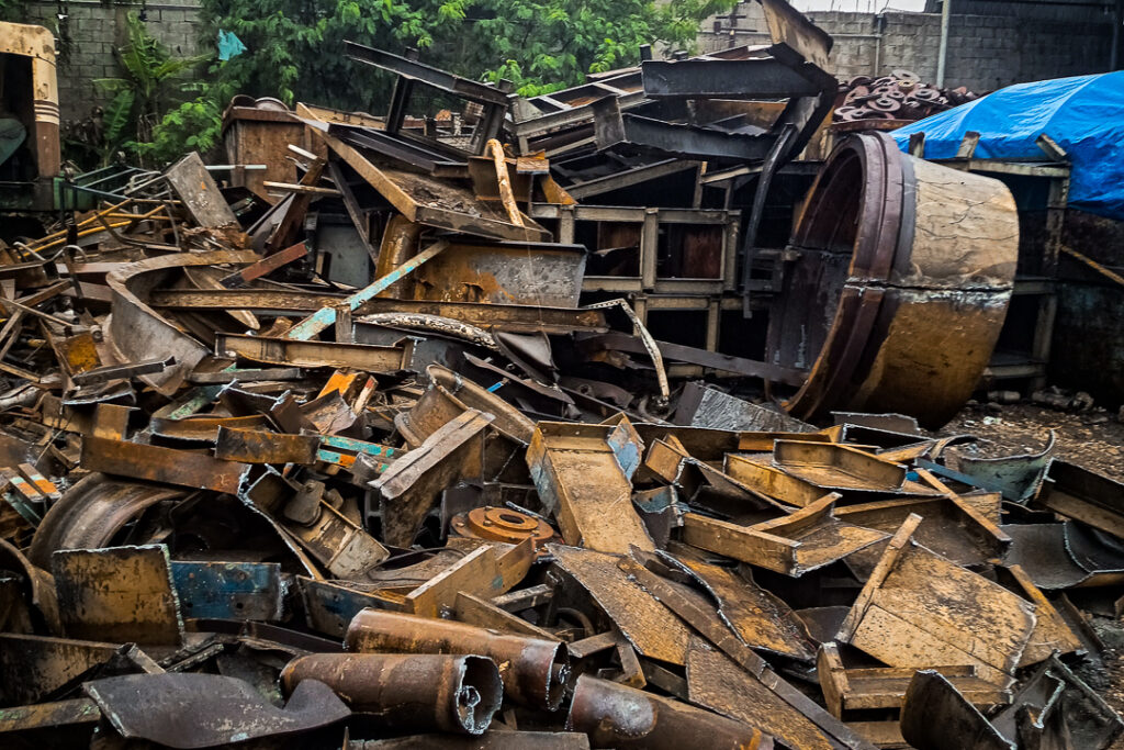 Sucata de obsolescência ferrosa — peças veiculares, componentes mecânicos e equipamentos desativados — separados por categoria no pátio da Sulfermetal. Fotografia autoral por Luyza Santos.